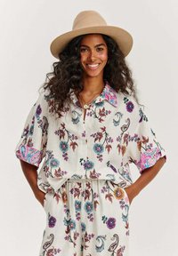 Košile s květinovým vzorem, krátký rukáv, vyrobena z lehké tkaniny s knoflíkovou léga a barevnými akcenty na límci a manžetách. Spárována s odpovídajícími kalhotami.