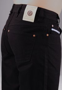 Schwarze Denim-Jeans mit hoher Taille, kupferner Hardware, zwei Gesäßtaschen und einem Markenstoffetikett an der Taille.