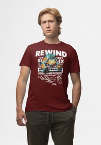 Bordová bavlněná tričko s bílým grafickým textem a barevnou, stylizovanou ilustrací postavy na přední straně. Krátké rukávy a kulatý výstřih.