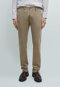 Beige chinos lavet af bomulds twill, med en lige ben design, forlommer og en enkelt knaplukning, parret med brune sko.