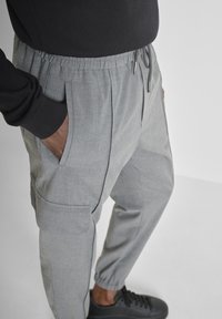 Grijze, lichte joggers met een elastische tailleband, zijzakken en taps toelopende benen. Gepaard met zwarte, lage sneakers.