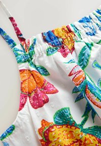Primer plano de tela blanca con estampado floral colorido, con detalle elástico fruncido y tirantes delgados.