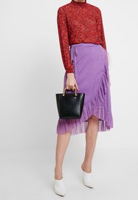 Červený květinový top s dlouhým rukávem, fialová asymetrická sukně s volánky, černá kabelka se zlatými úchyty, bílé lodičky s špičatou špičkou.