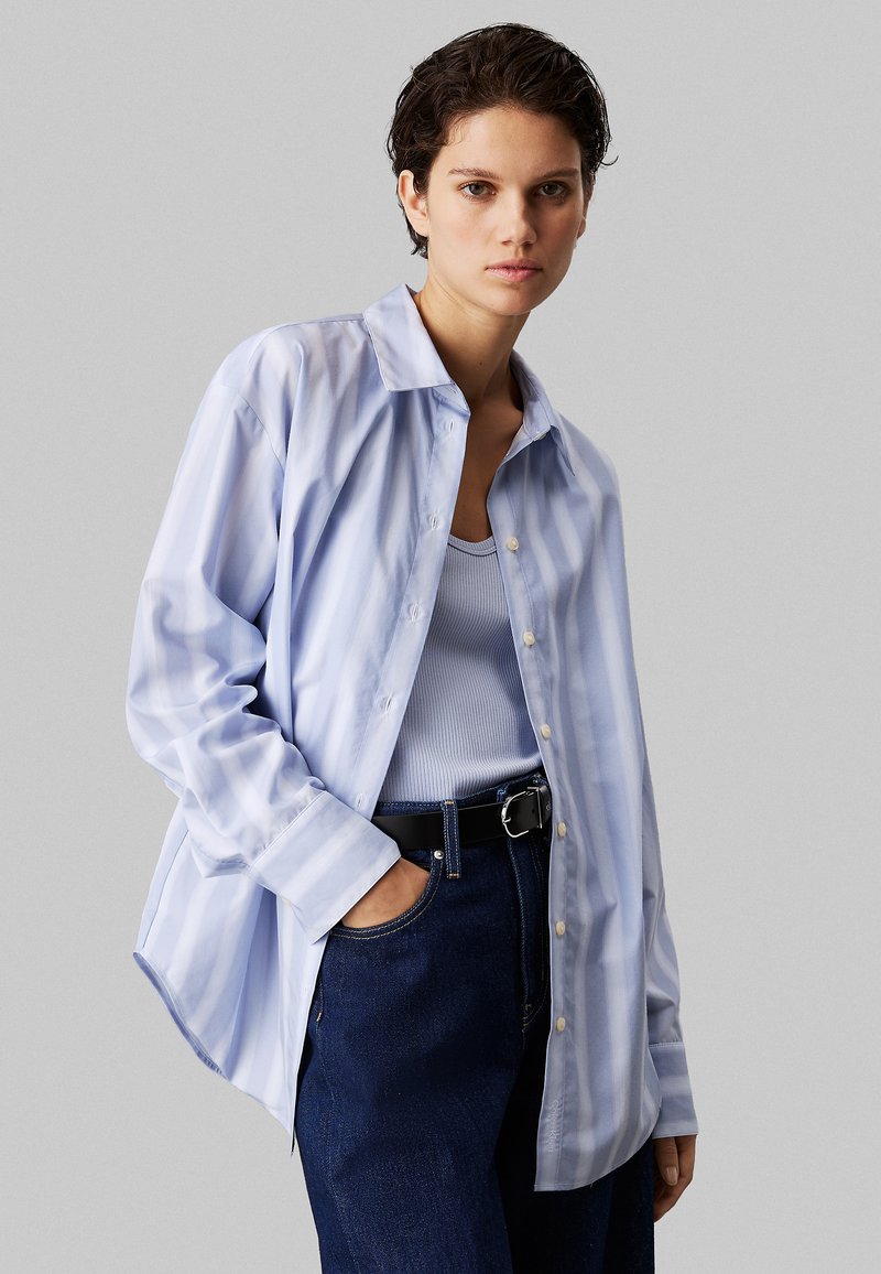 Lyseblå stribet skjorte med krave, lange ærmer, og en afslappet pasform, parret med en tætsiddende blå top og mørke denim jeans.