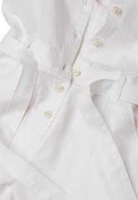 Abito bianco in lino con una parte anteriore con bottoni, vita cintrata e texture liscia. Presenta cuciture decorative e piccoli bottoni.