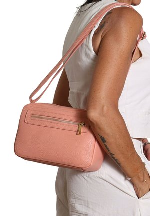 Donna che indossa una canotta bianca senza maniche e pantaloni, con una borsa rosa testurizzata con tasca frontale con zip sulla spalla.