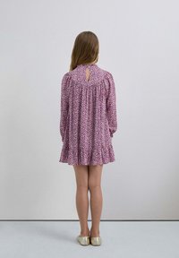 Vestido con estampado floral en tonos de rosa y blanco, de mangas largas, detalle de abertura en la espalda, con dobladillo con volantes, combinado con bailarinas doradas brillantes.
