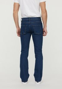 Jean évasé bleu foncé avec un design classique à cinq poches. Matériau en denim robuste avec une texture lisse et des détails de couture neutres.