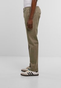 Pantalones de algodón verde oliva claro con un diseño de pierna recta, que cuentan con bolsillos frontales y una cinturilla con botón. Combinados con zapatillas blancas y negras.