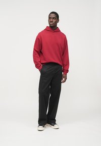 Punainen hupparipaita väljässä istuvuudessa, yhdistetty mustiin leveälahkeisiin housuihin ja valkopohjaisiin mustiin tennareihin. Yksinkertainen muotoilu, ilman näkyviä kuvioita.