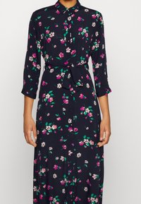 Námořnické květinové šaty vyrobené z lehkého materiálu, s knoflíkovým zapínáním vpředu, tříčtvrtečn ími rukávy, zavazovacími v pase a růžovými a zelenými květinovými vzory.