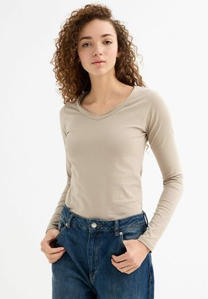 Camisa de manga larga color beige claro con un diseño de escote en V, hecha de una tela suave. Combinada con jeans de mezclilla azul de tiro alto.