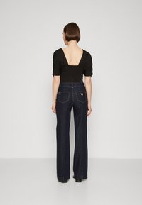 Top nero con scollatura a V profonda, abbinato a jeans a gamba larga blu navy con due tasche posteriori e un piccolo dettaglio con logo triangolare.