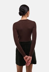Haut long à manches ribbées marron associé à une jupe en velours côtelé vert foncé. Le vêtement présente un design près du corps et un col rond.