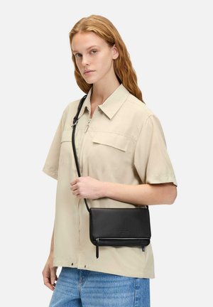 Black leather crossbody bag with a zip closure and side zipper detail, rectangular shape, and smooth texture. Worn by a model with light clothing.