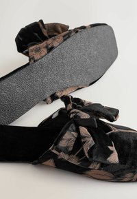 Schwarze Stoff-Slipper mit floralen Mustern in Beige und einem Schleifenakzent. Strukturiertes Gummisohle für besseren Halt.