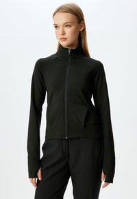 Chaqueta negra con cremallera y cuello alto, hecha de un tejido suave y elástico. Presenta mangas largas y bolsillos laterales. Diseño minimalista.
