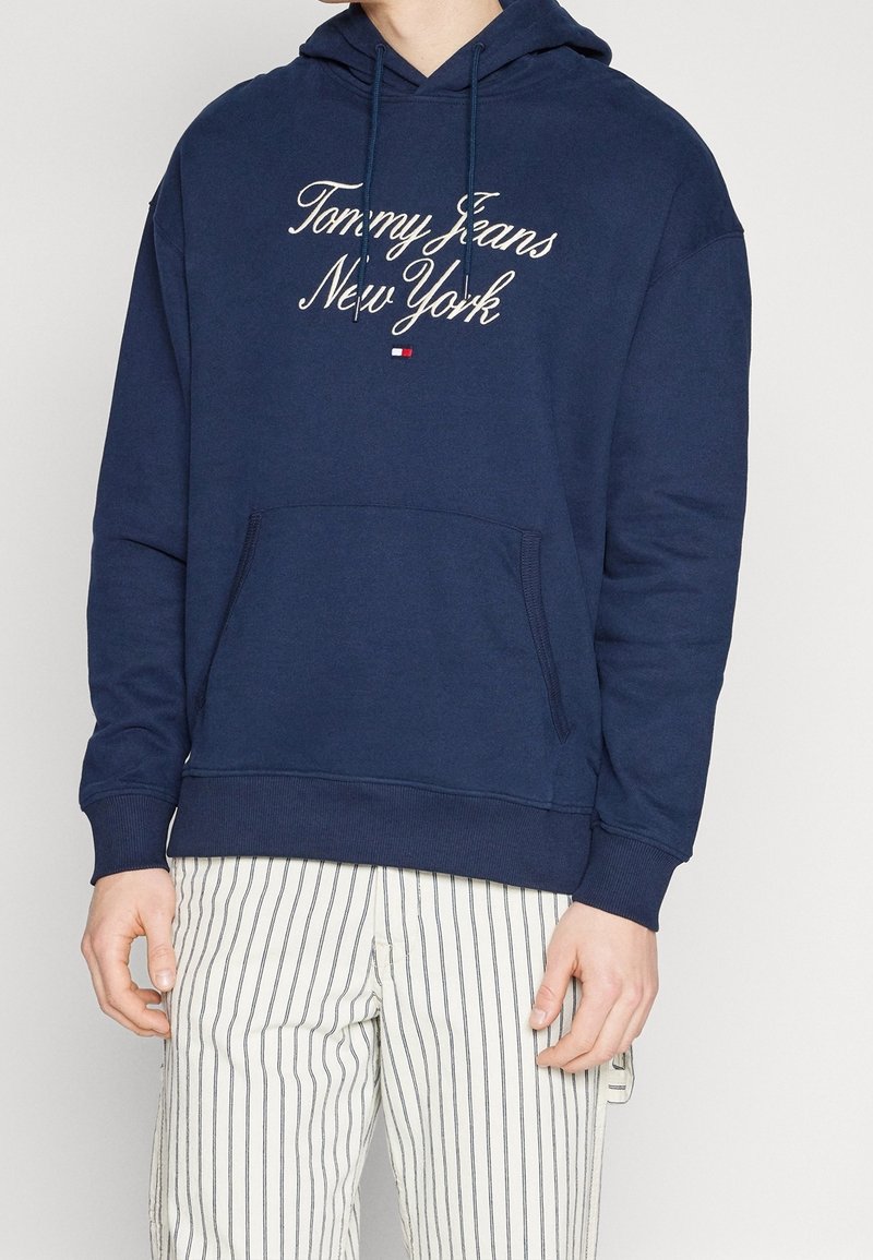 Sweat à capuche bleu marine avec poche avant, capuche à cordon et texte brodé "Tommy Jeans New York". Tissu doux, avec poignets et ourlet côtelés.