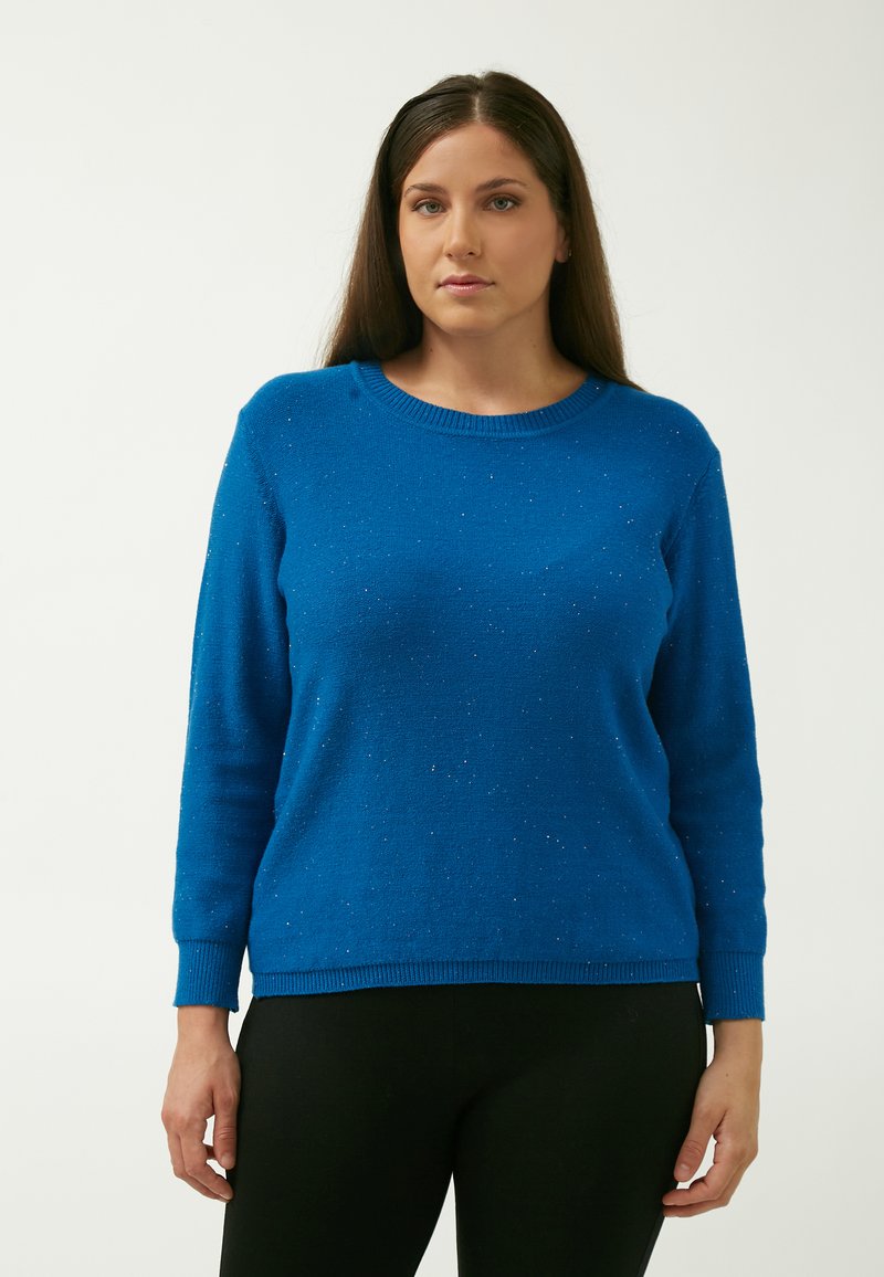 Blå sweater med lange ærmer, rund hals og subtile glitrende detaljer. Blød tekstur, ribbede manchetter og kant, parret med sorte bukser.
