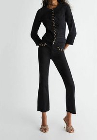 Veste en denim noir avec quincaillerie dorée et un design ajusté. Associée à un jean noir évasé avec des accents de rivets. Silhouette ajustée.