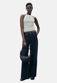 Striped halter top paired with wide-leg dark denim jeans. Model holds a black curved handbag. Simple design, light and dark color contrast.