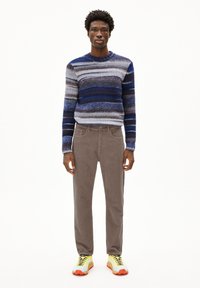 Gestreifter Strickpullover in Blau- und Grautönen, kombiniert mit braunen Cordhosen und leuchtend gelben Turnschuhen mit orangefarbenen Details.