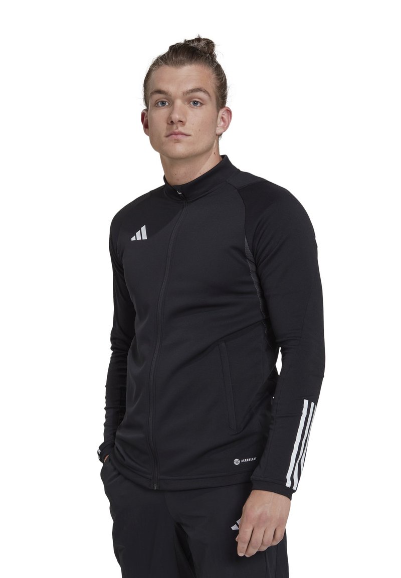 Schwarze Sportjacke mit hohem Kragen, Reißverschluss, Seitentaschen und weißen Streifen an den Ärmeln. Hergestellt aus glattem, dehnbarem Stoff.
