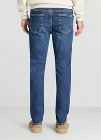 Jean denim bleu à coupe droite, avec deux poches arrière et des détails de couture subtils, assorti à des chaussures en suède beige.