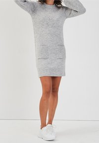 Robe pull gris en maille avec un col rond, des épaules tombantes, deux poches avant et des détails perforés en chevrons sur la poitrine.