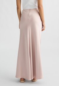 Lunga gonna rosa realizzata in tessuto morbido, con zip nascosta sul retro e una forma svasata che scivola delicatamente fino a terra.