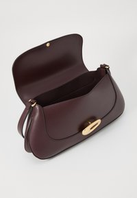 Sac à main en cuir bourgogne avec une texture lisse, des accessoires en or, une forme arrondie et une fermeture à bouton magnétique donnant accès à un intérieur spacieux.