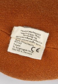 Oranžová textilná etiketa so tkanou štruktúrou, ktorá uvádza zloženie materiálu a pokyny na starostlivosť v obdĺžnikovom tvare s bielym písmom.