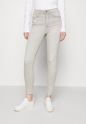 Jeans skinny grigi chiaro con dettagli strappati e orli sfrangiati. Realizzati in denim con una texture liscia. Abbinati a sneakers bianche.