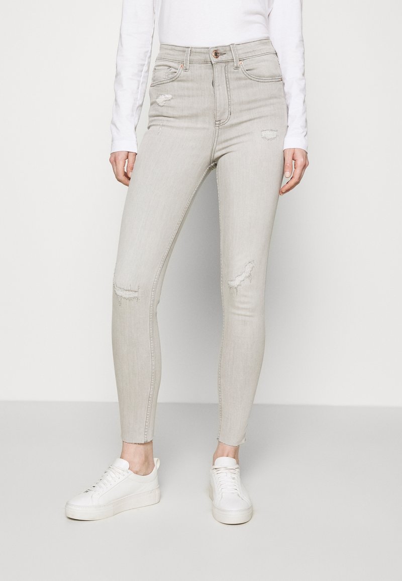 Jeans ajustados de color gris claro con detalles desgastados y bajos deshilachados. Fabricados en denim con una textura suave. Combinados con zapatillas blancas.