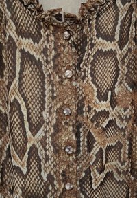 Tissu imprimé serpent marron et beige avec une rangée centrale de boutons ronds et un détail d'encolure froncée.