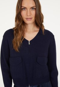 Marinefarbener Zip-Cardigan aus weichem Strickstoff, mit V-Ausschnitt, zwei Fronttaschen und geripptem Saum.