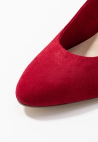 Scarpa con tacco alto in suede rosso, a punta e con un profilo a bassa scollatura, dotata di una fodera interna liscia e una suola esterna discreta.