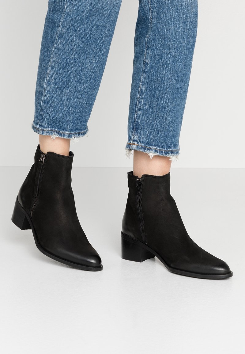 Botines de ante negro con punta afilada y pequeño tacón cuadrado. Cuentan con cremalleras laterales y un diseño elegante para un uso fácil.
