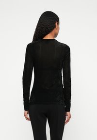 Camisola preta de manga longa feita de um tecido suave e texturado. Apresenta um decote redondo simples e uma silhueta ajustada, com um design detalhado nas mangas.