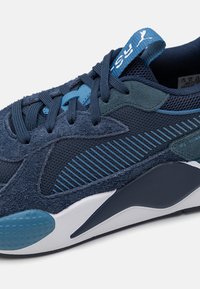 Baskets bleu marine en mélange de suède et de mesh, avec des accents blancs et turquoise, une semelle texturée et des détails à rayures.