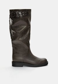 Knee-high ruskeat nahkasaappaat, joissa on teksturoitu pinta, koristeellinen hihna ja solki metallisilla yksityiskohdilla sekä litteät mustat pohjat.
