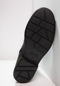 Suela de zapato negra con goma texturizada, presenta un patrón de banda de rodadura geométrica y el logo grabado "CAMPER 42", diseño plano para estabilidad.