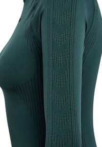 Langsleeve sporttop in donkergroene stof. Heeft een textuurpatroon met kleine perforaties en een fitted ontwerp.