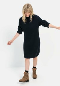 Marineblaues ribbenstrick Kleid mit hohem Kragen und oversized Ärmeln, kombiniert mit hellbraunen Schnürstiefeln und schwarzen Socken.