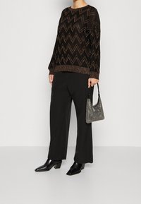 Pull-over noir avec un motif en zigzag métallique, associé à un pantalon large noir et un sac à main métallique. Bottines noires à talons épais.