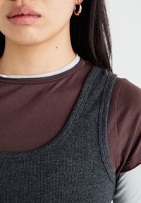 Gray ribbed tank top layered over a brown shirt with a light blue crew neckline. Features curved necklines and smooth textures.