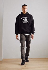 Black hoodie with white logo, gray cargo pants with side pockets, and black sneakers. Smooth textures against a light background.