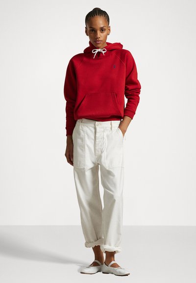 Rød hettegenser med lommer foran, kombinert med hvite cargo-bukser med oppbrett og hvite slip-on sko.