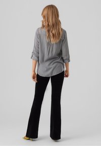 Pantalons noirs évasés associés à une chemise à boutons rayée avec des manches retroussées. La chemise a une texture lisse et un détail de renfort au dos.