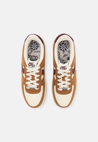 Ténis de camurça castanha com biqueira e entressola de couro branco, detalhes roxos e forro com impressão gráfica. Apresentam um design tradicional de atacadores.